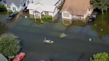 In an aerial image, two men drive a boat down a flooded residential street. 