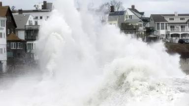A large wave crashes ashore onto a row of homes
