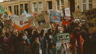 A large crowd of young protesters with signs crowd a street in Glasgow