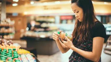 A young woman reading a bottled juice drink label as she shops for groceries in a supermarket.