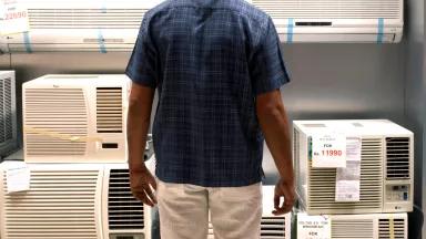 A man looking at shelves of air conditioners (ACs) for sale in a store.