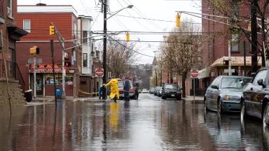 A person in a yellow raincoat stands in the middle of a flooded intersection