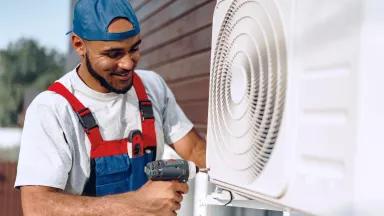 A smiling man installing an air conditioner using a power drill