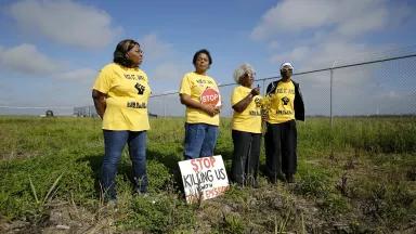 Four women in yellow t-shirts stand on one side of a chainlink fence