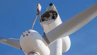 A crane lifts the blades of a wind turbine to attach it to its column