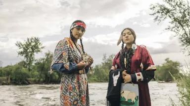 Two women stand next to a rushing river