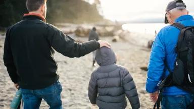 Two adults and a child walk along a sandy shoreline