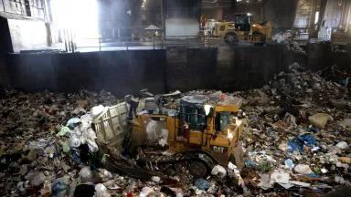 A yellow Cat bulldozer pushes around mounds of plastic garbage at a facility