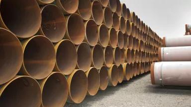 Large sections of piping are stacked in multiple rows