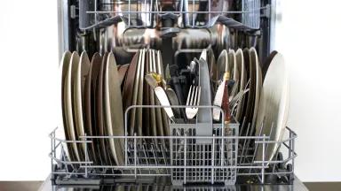 An open dishwasher full of plates and silverware