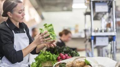 A chef in a professional kitchen handles bundles of fresh produce