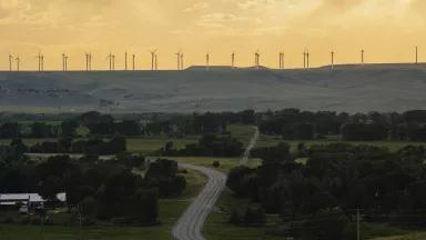 A row of wind turbines stand along a ridge above a rural area