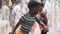 Two young children playing in sprinklers in Domino Park, Williamsburg, Brooklyn, New York