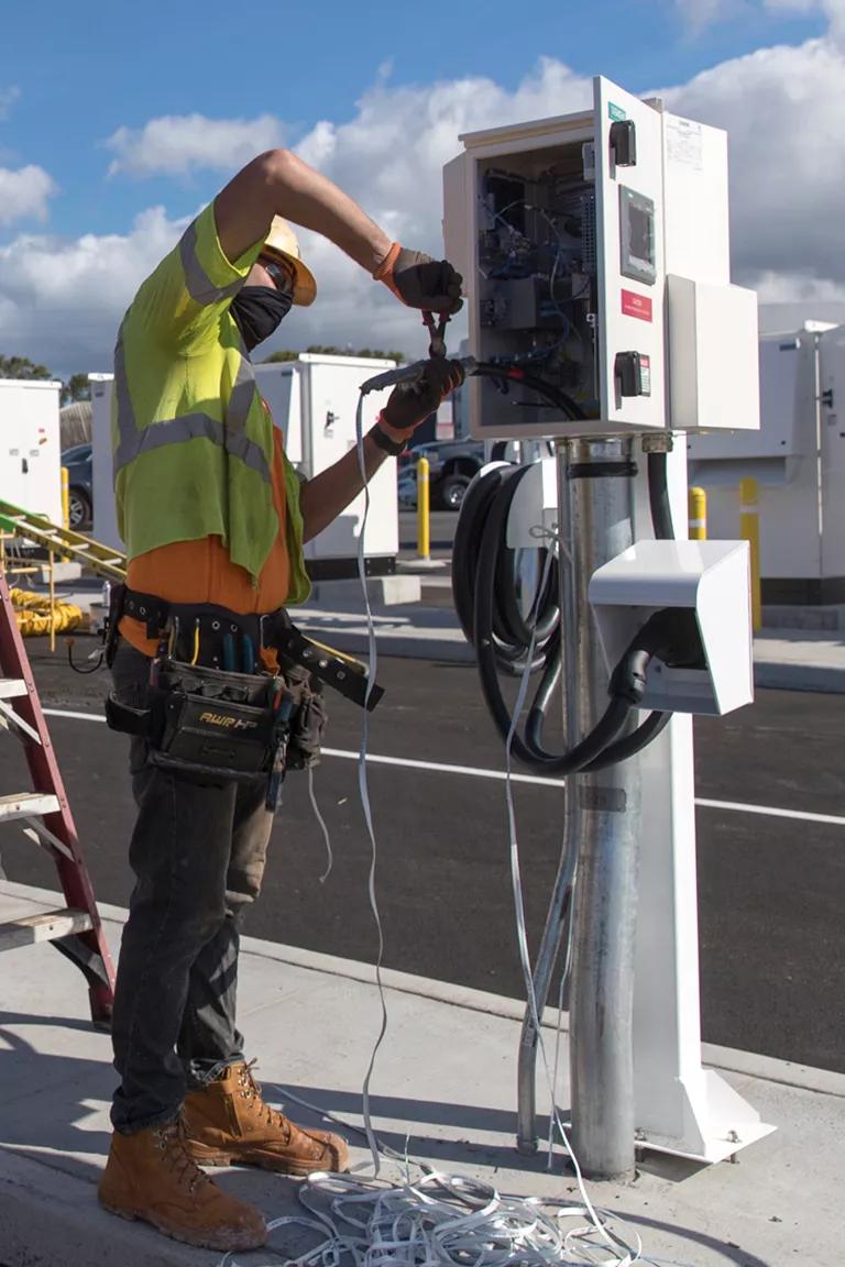 A worker using pliers on the wiring of an electric bus charging station