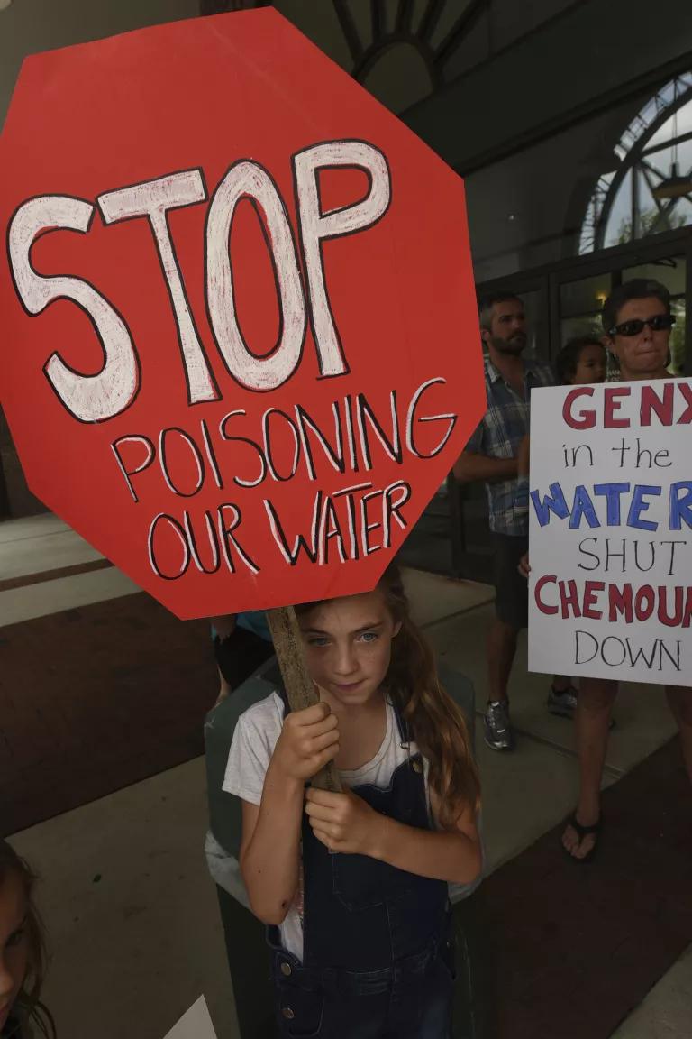 A child holding up a big red sign that says "Stop poisoning our water"