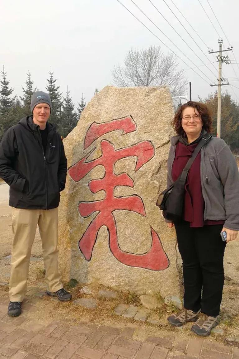 Two people stand on either side of a large stone with a Chinese character painted on it in red